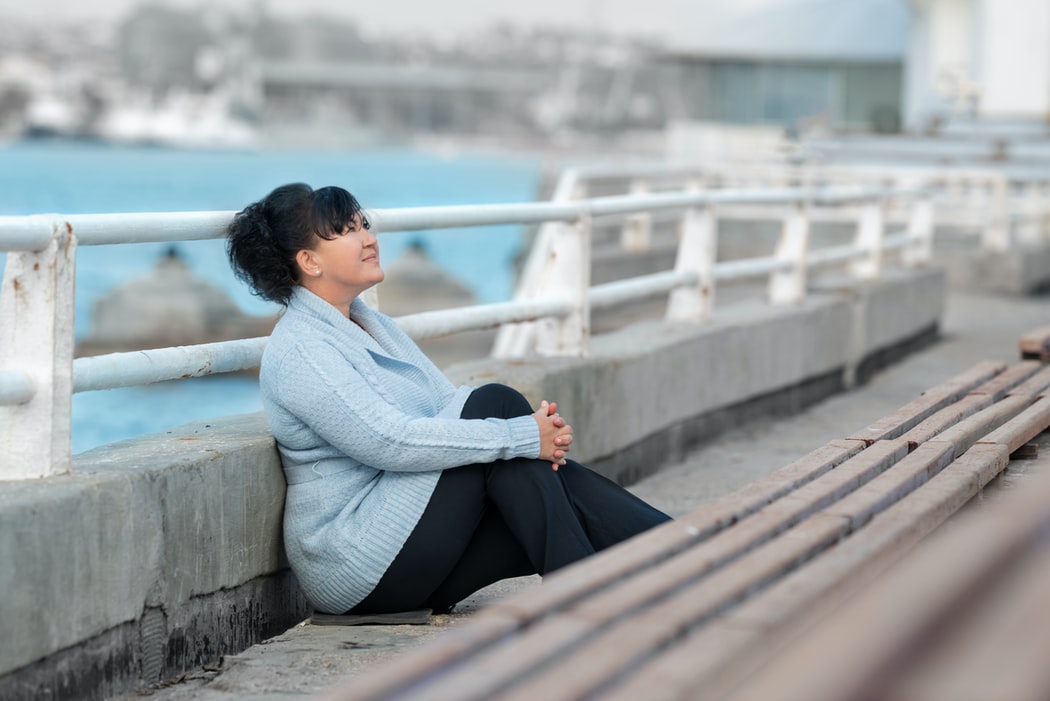 桟橋で膝を抱え空を見ている女性